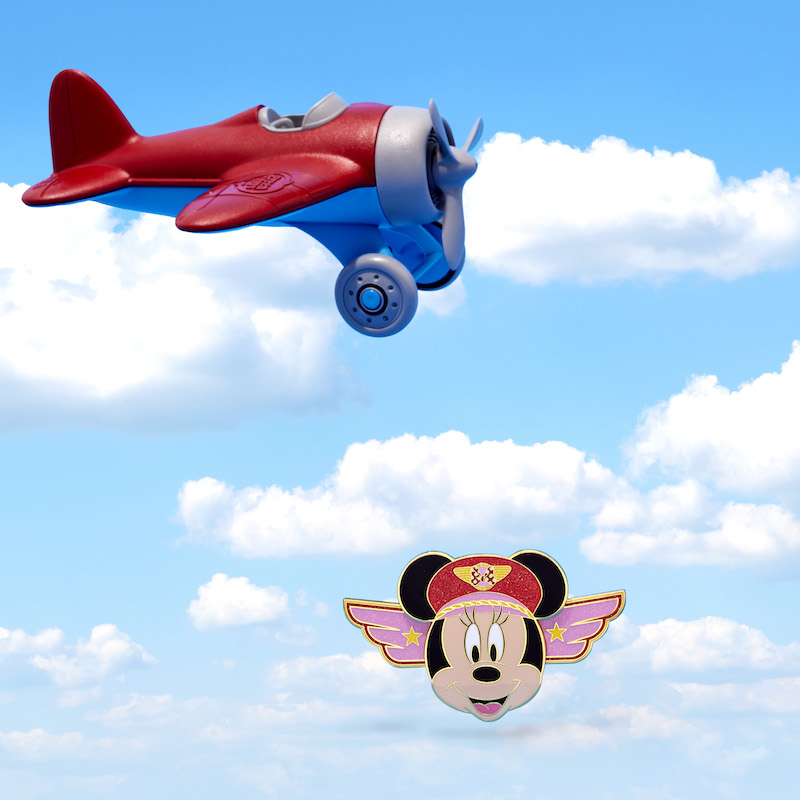 Limited Edition Loungefly Minnie Mouse Pilot Pin floating against a background that looks like the sky with a red and blue airplane flying above it.